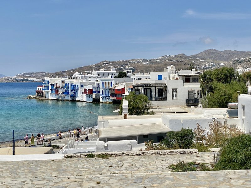 Colorful, historic houses line the waterfront in Little Venice, Mykonos, with the Mediterranean Sea in the background.