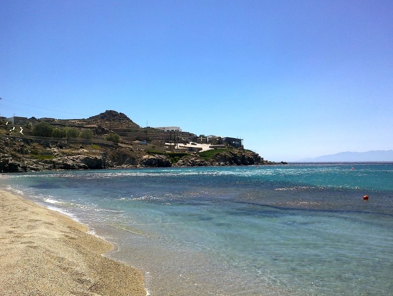 A serene beach scene at Paradise Beach in Mykonos, with clear blue waters and sunbathers relaxing on the sand.