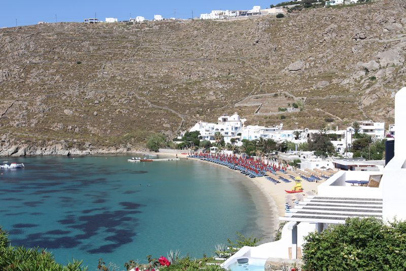 A serene beach scene at Platis Gialos, Greece, with clear blue waters and a sandy shore.