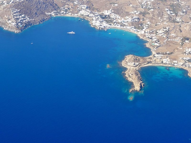 A serene beach scene at Platis Gialos on the Greek island of Mykonos, with clear waters and a sandy shore.