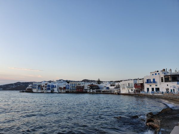 Restaurant tables and chairs set out along the water's edge in Little Venice, Mykonos, at dusk