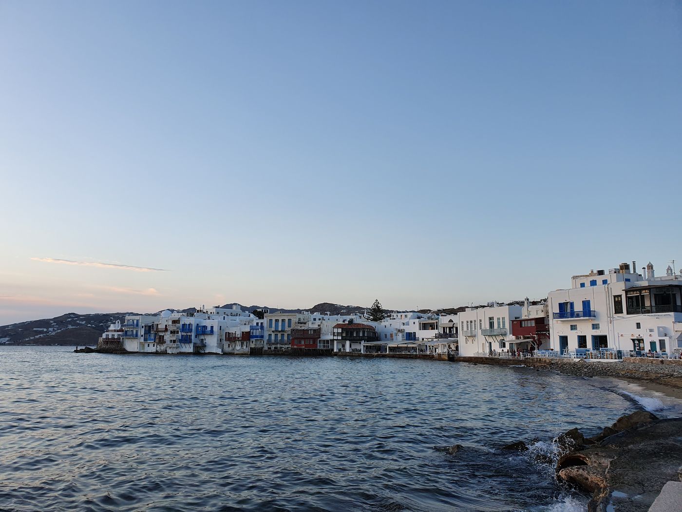 Restaurant tables and chairs set out along the water's edge in Little Venice, Mykonos, at dusk