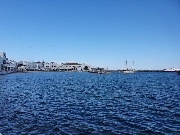 Caiques and a traditional wooden boat moored in Mykonos old port with the whitewashed town behind