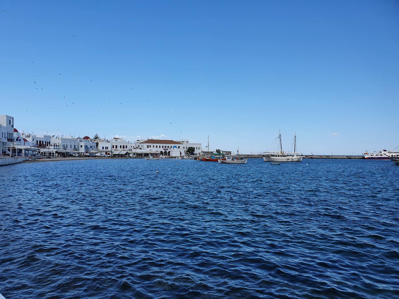 Caiques and a traditional wooden boat moored in Mykonos old port with the whitewashed town behind