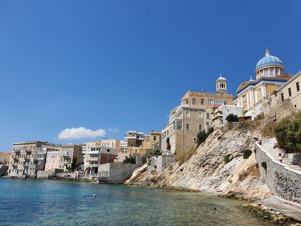 Neoclassical waterfront buildings in Ermoupoli, Syros, with the blue-domed church of Agios Nikolaos above the sea
