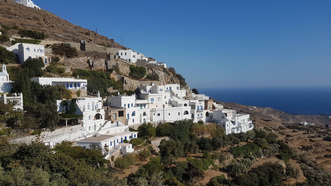 A whitewashed hillside village on Tinos with terraces of houses running down to the sea