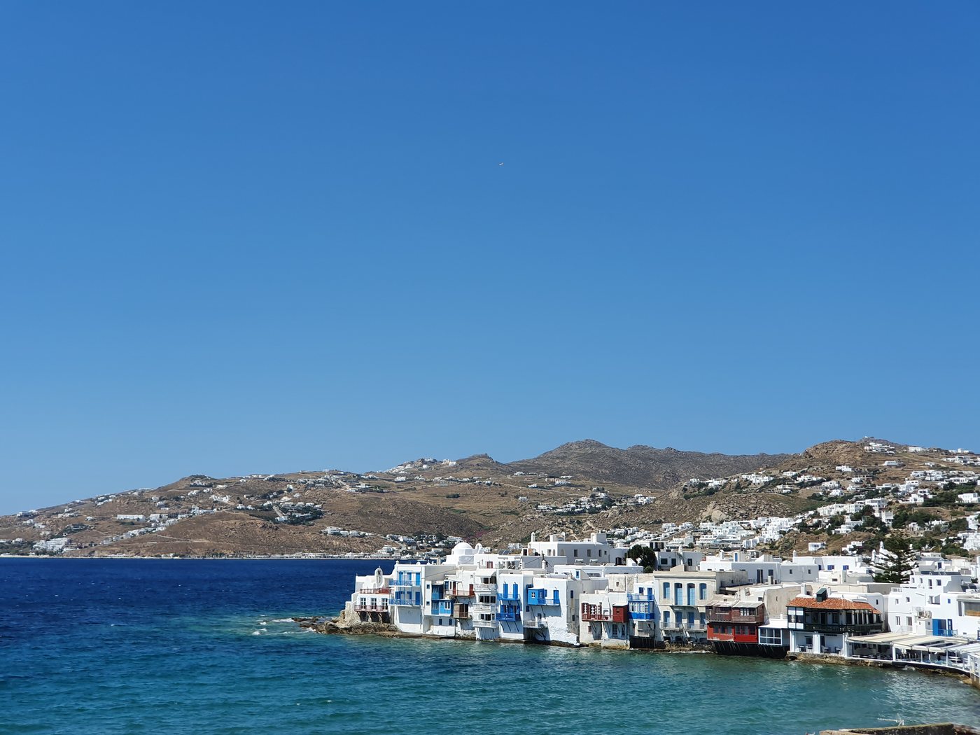 A wide view of Mykonos town rising up the hillside above the deep blue harbour