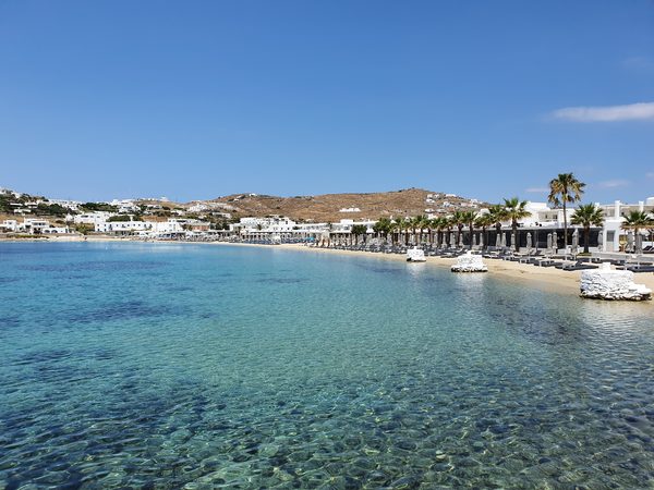 The curved sandy bay at Ornos beach, lined with palm trees and beach club sunbeds