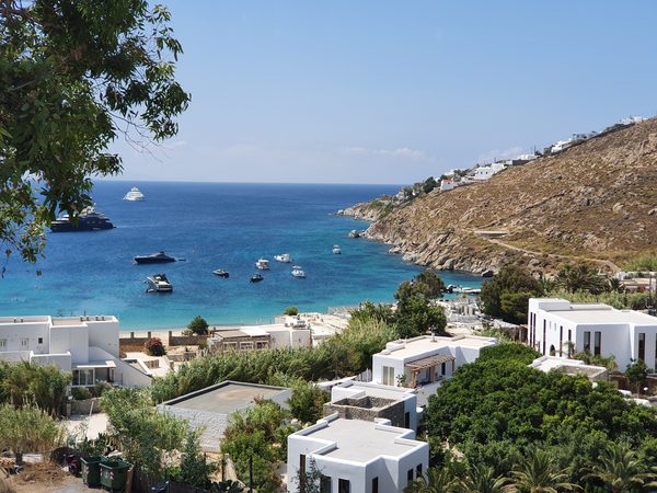 An elevated view over Psarou's small cove, with yachts anchored in the clear water and white villas on the hillside above
